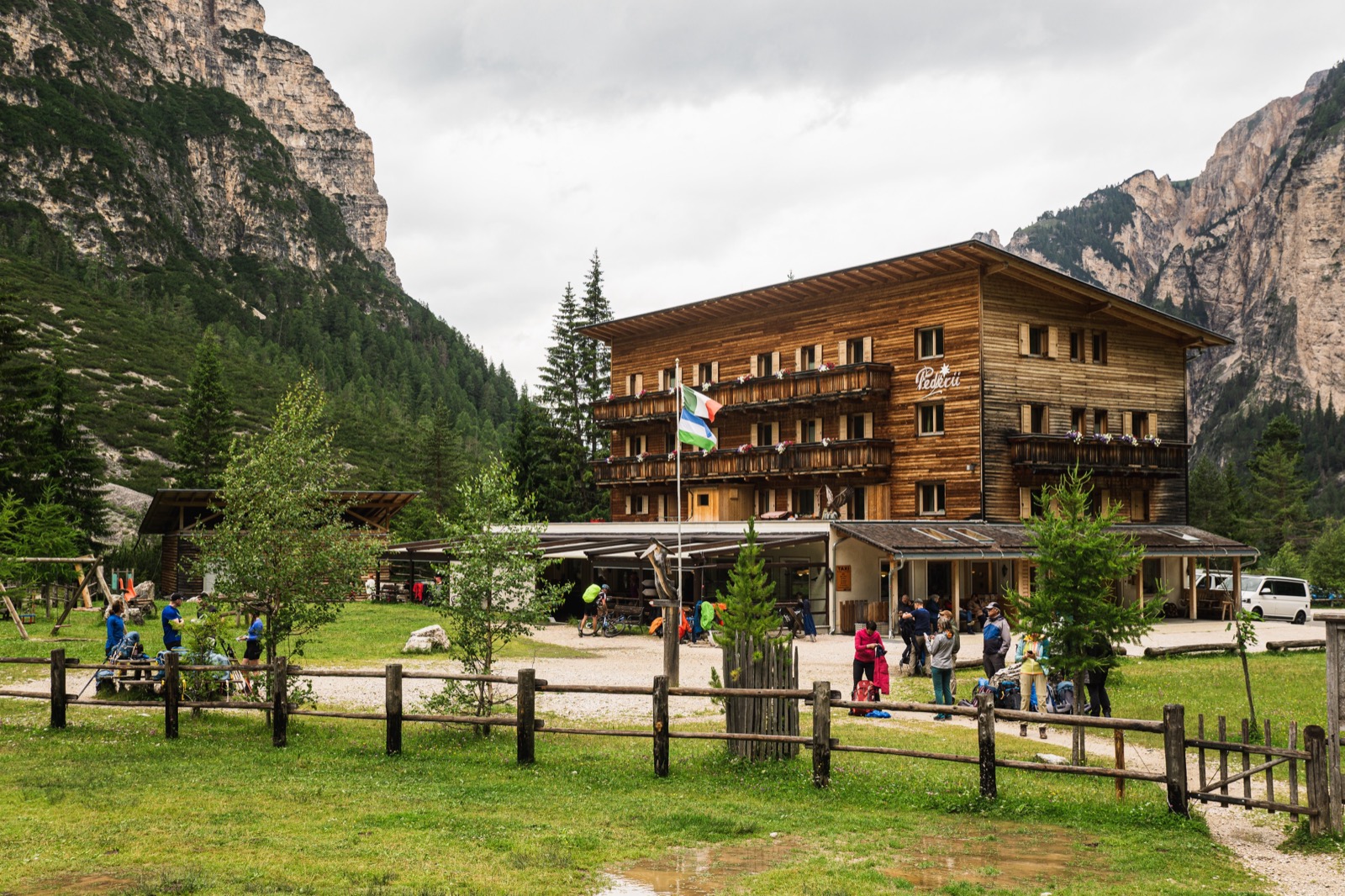 Large wooden mountain hut flying a flag beneath pale Dolomite cliffs