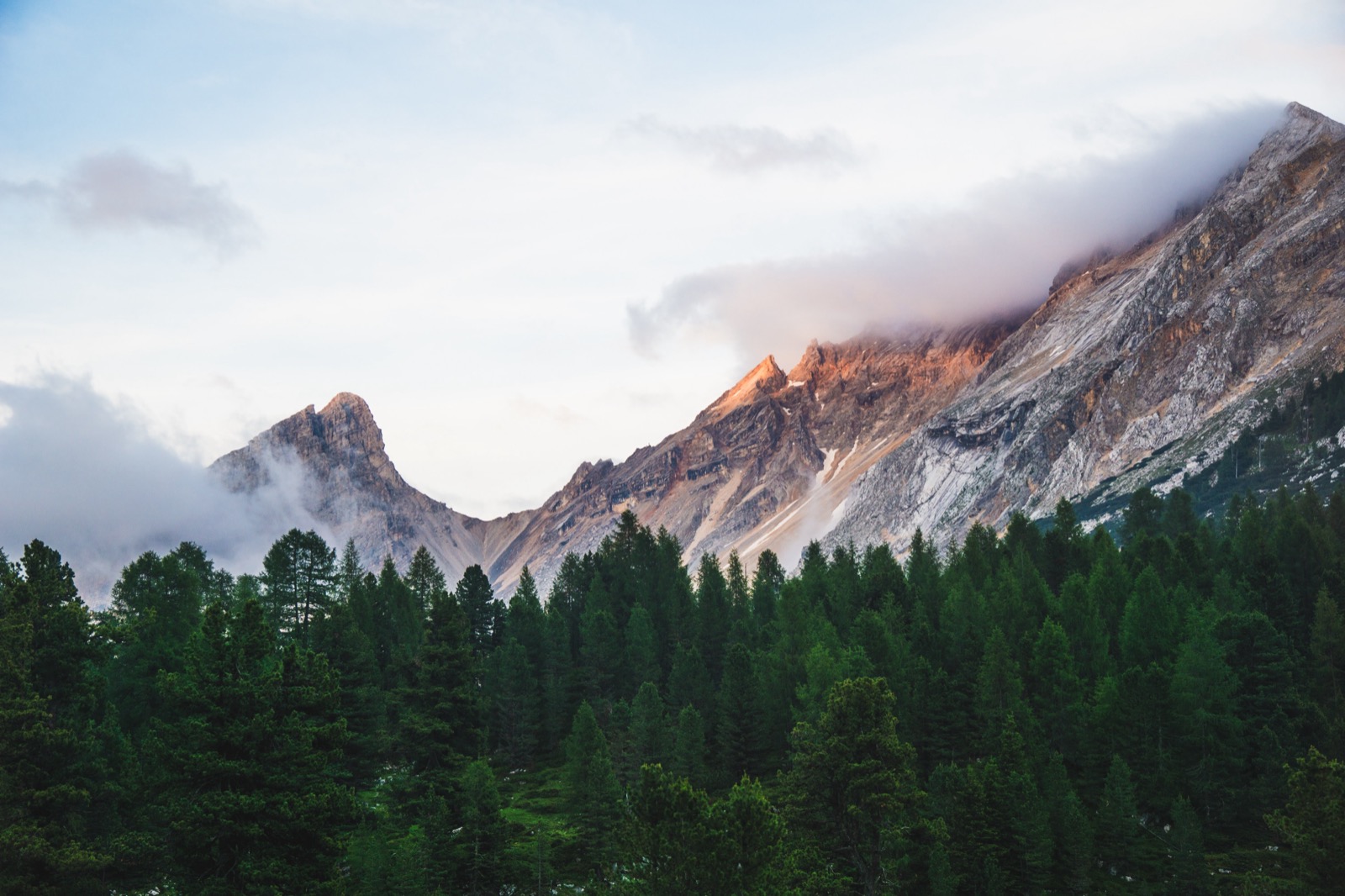 Dolomite peaks catching soft evening light above a dark pine forest