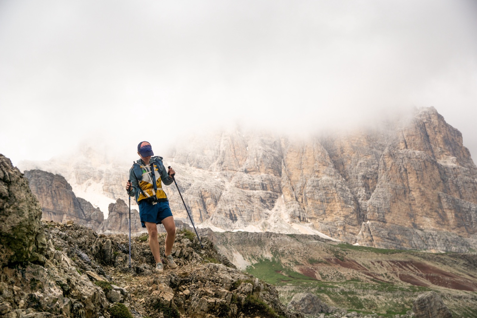 Runner with poles on a rocky ridge, Dolomite walls rising into the clouds behind