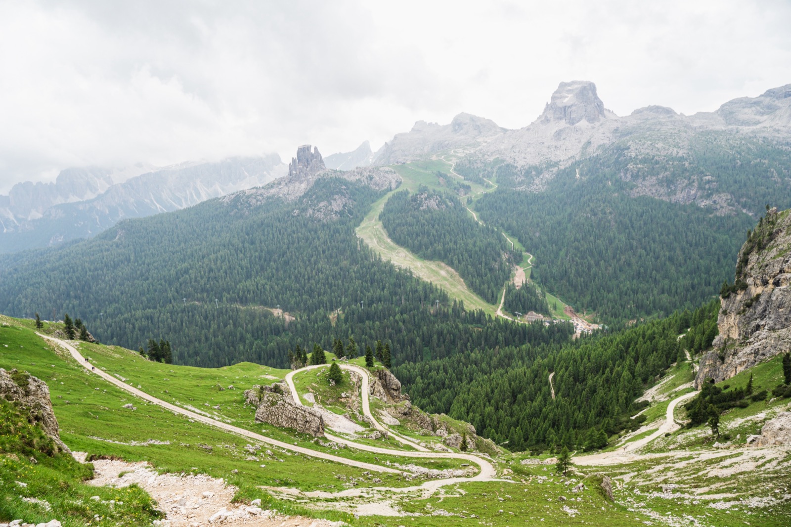 Gravel trails winding through green Dolomite valleys under misty peaks
