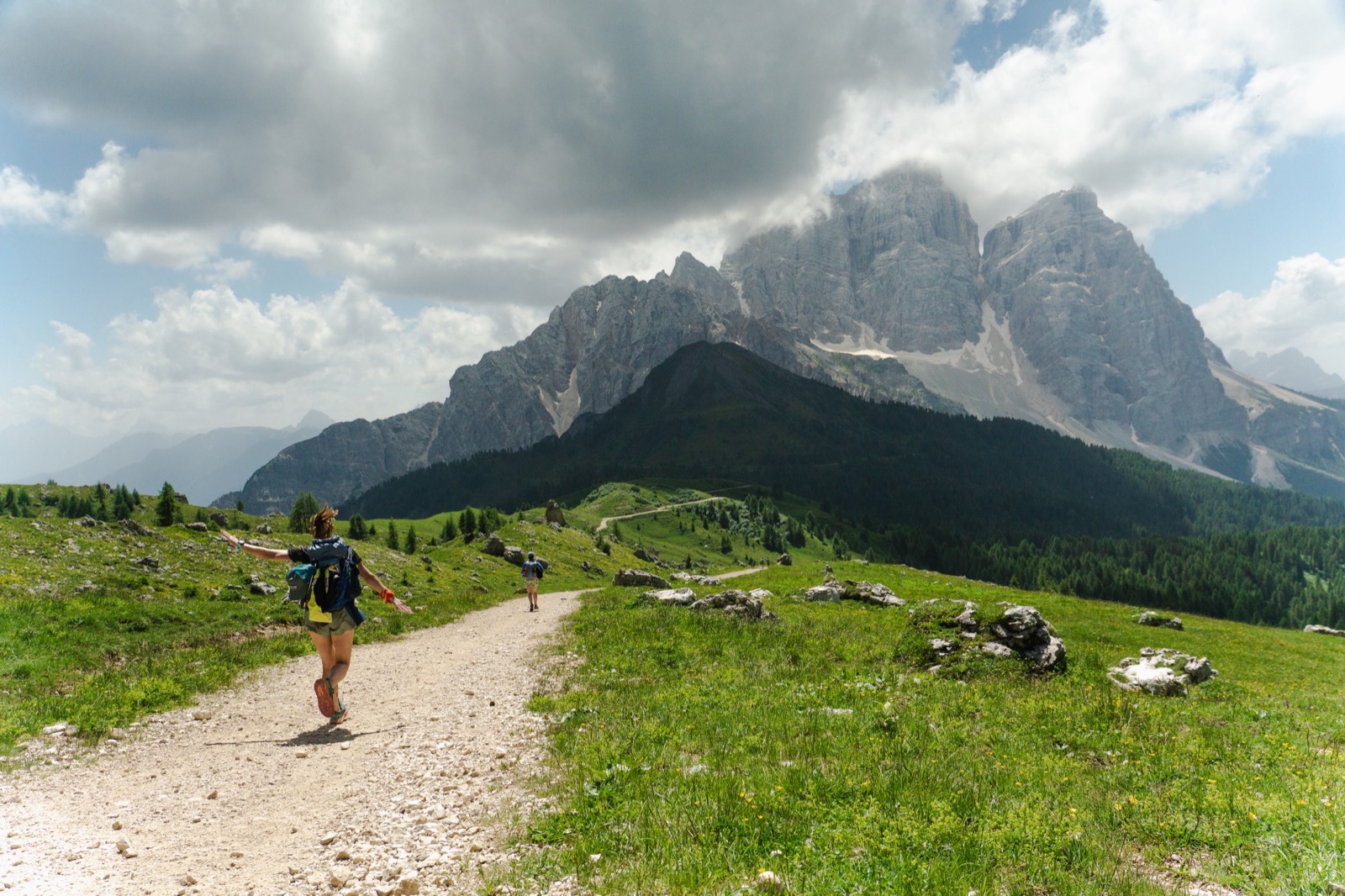 Runner with arms outstretched on a gravel path toward jagged Dolomite peaks