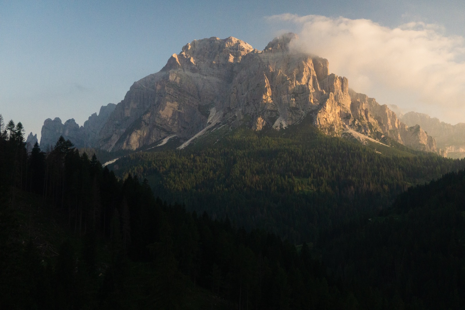 Sunlit Dolomite massif above a shadowed forest at dusk