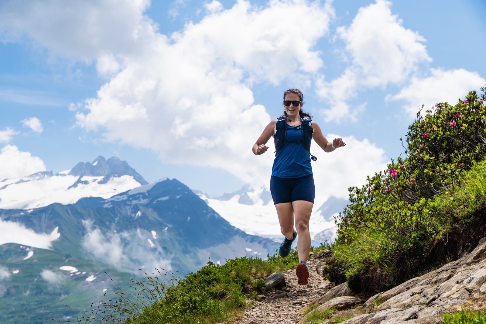 Smiling runner on a rocky trail with snowy peaks and big clouds behind