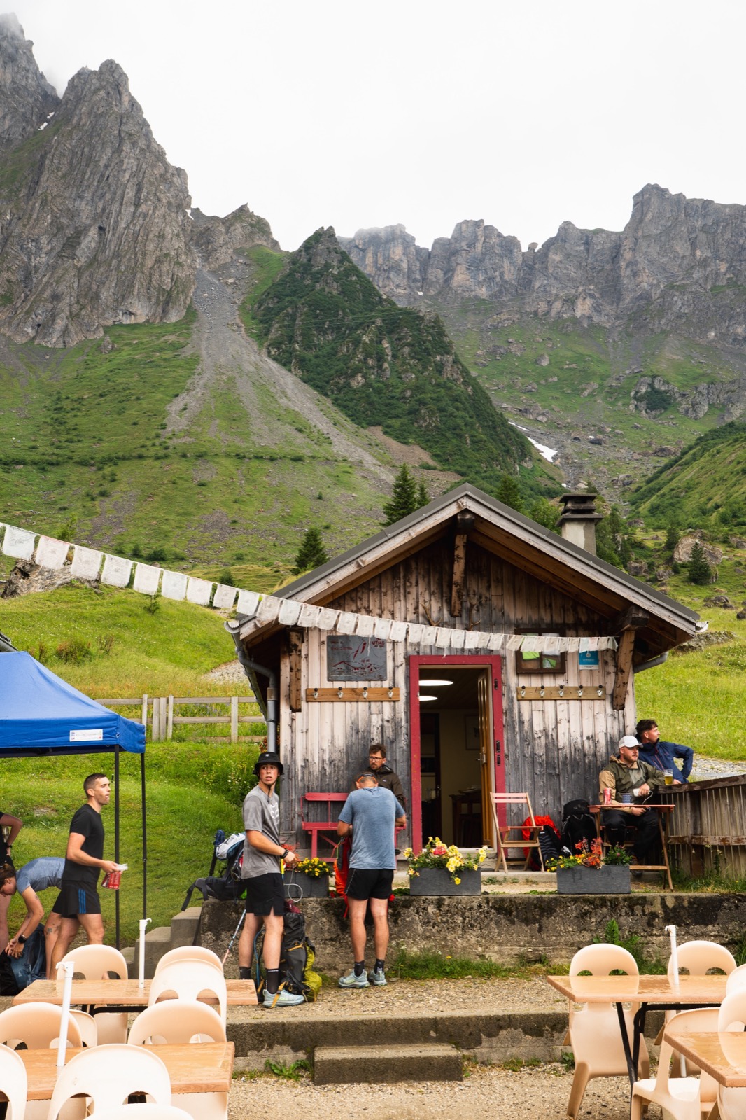 Runners resting outside a small mountain hut below craggy peaks