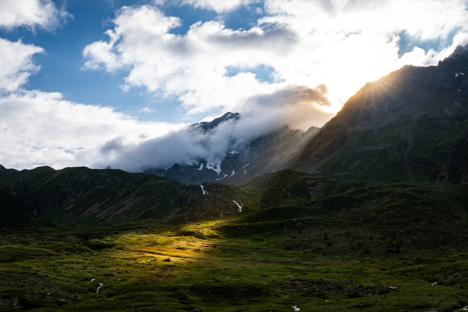 Sunbeams breaking through clouds over a green alpine valley