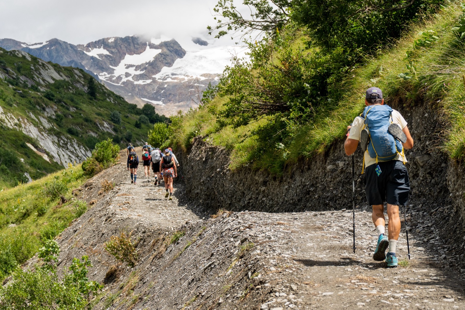 Line of runners on a balcony trail with snowy peaks in the distance