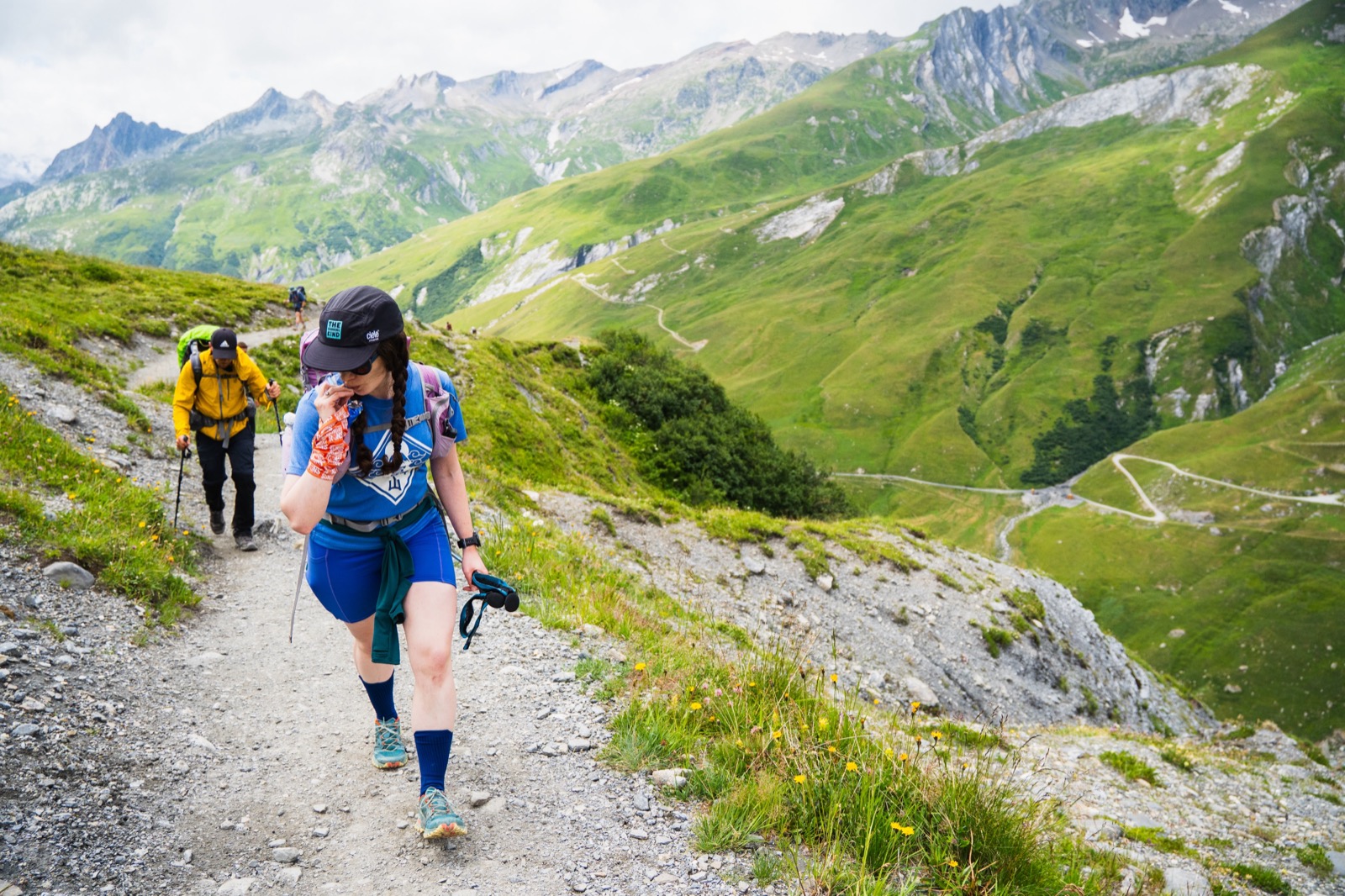 Runner on a rocky path high above a green valley with switchback roads below