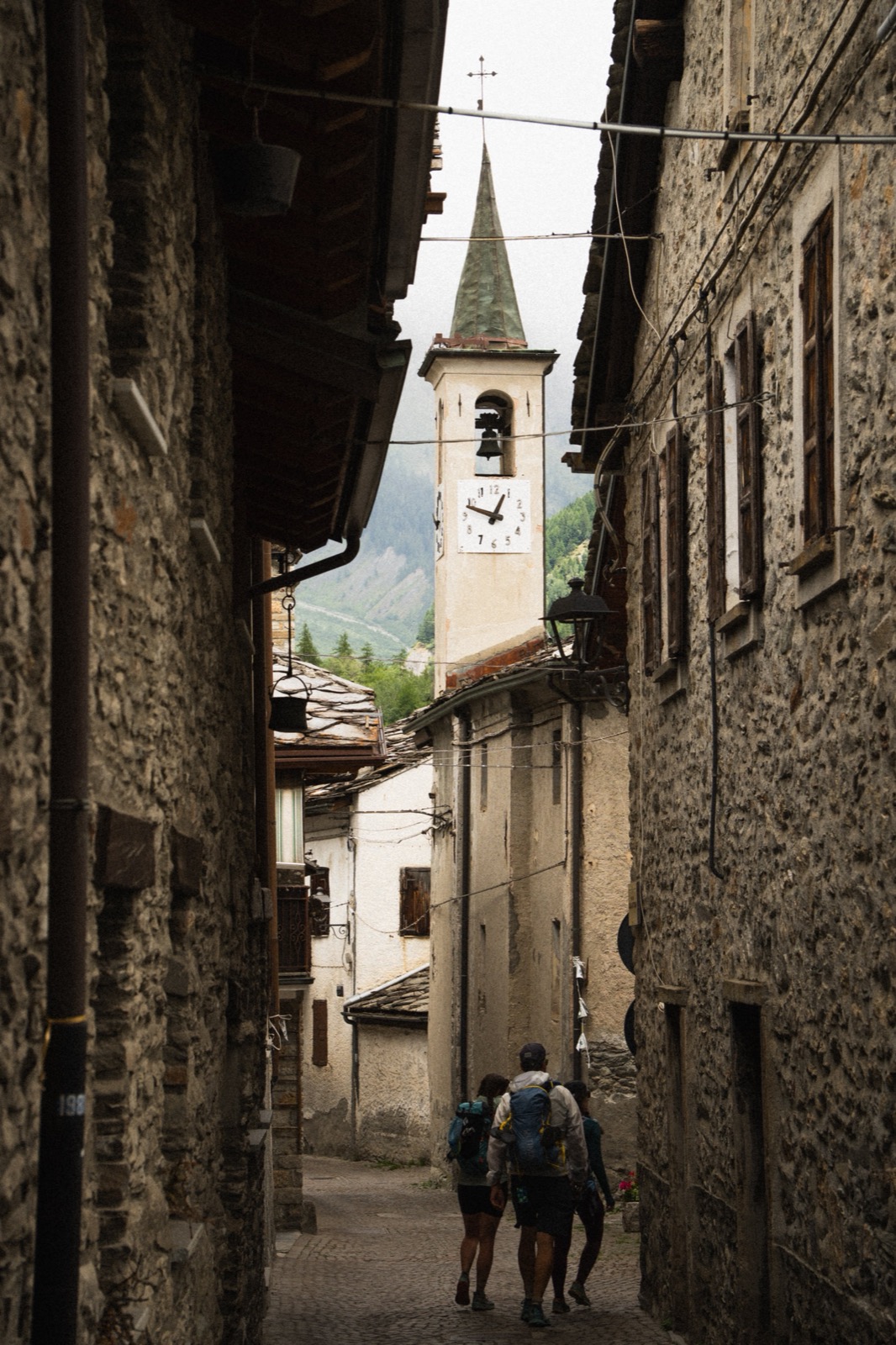 Runners walking a narrow stone lane toward a village bell tower