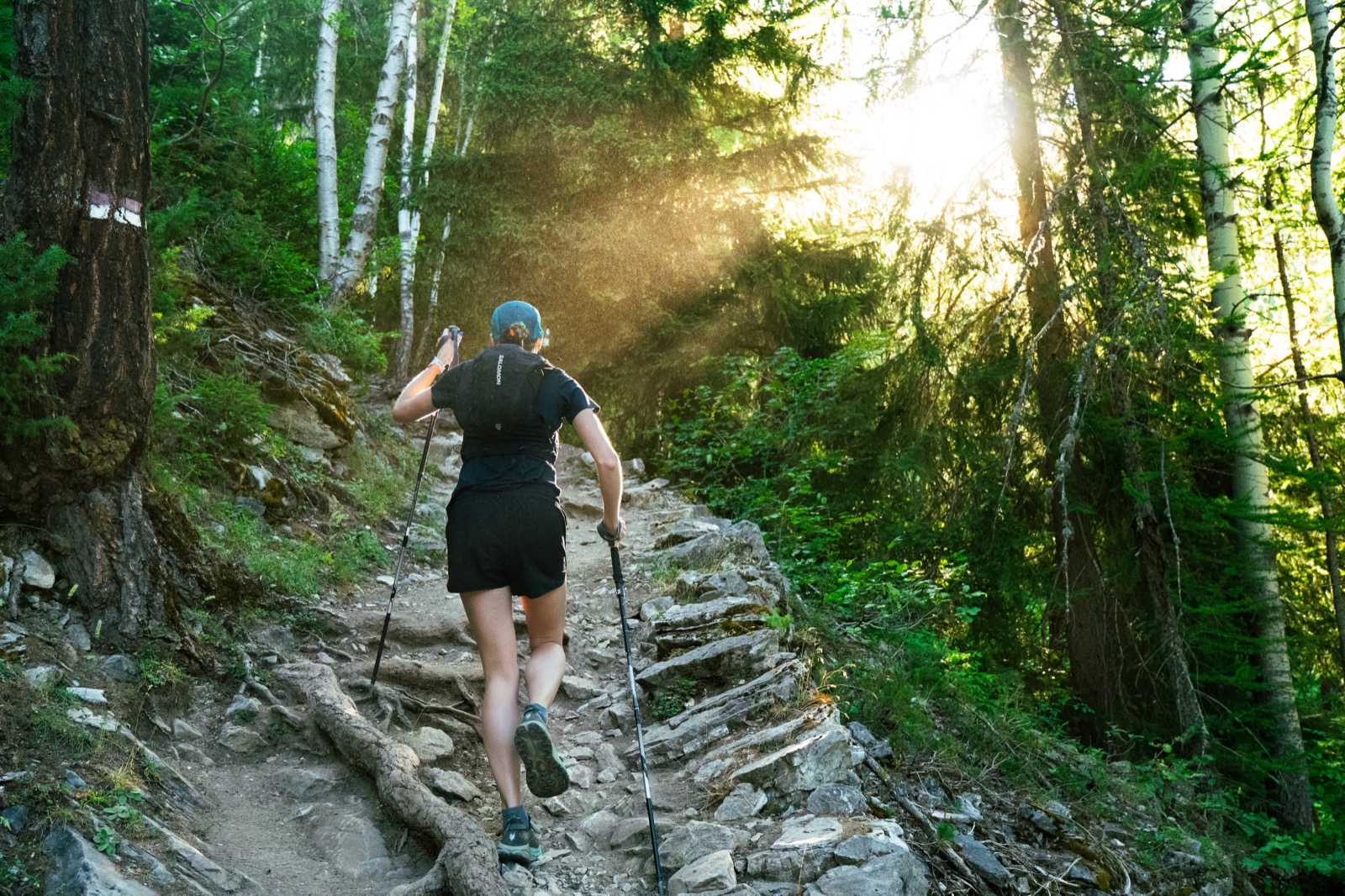 Runner climbing a rocky forest trail through rays of sunlight