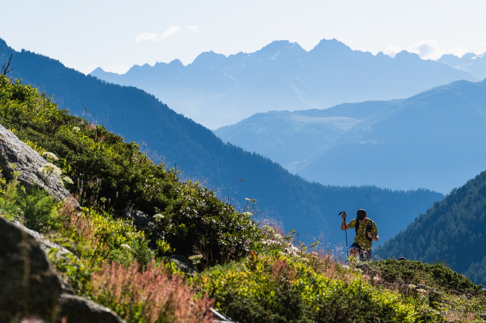 Runner with poles on a ridge above layered blue mountain ranges