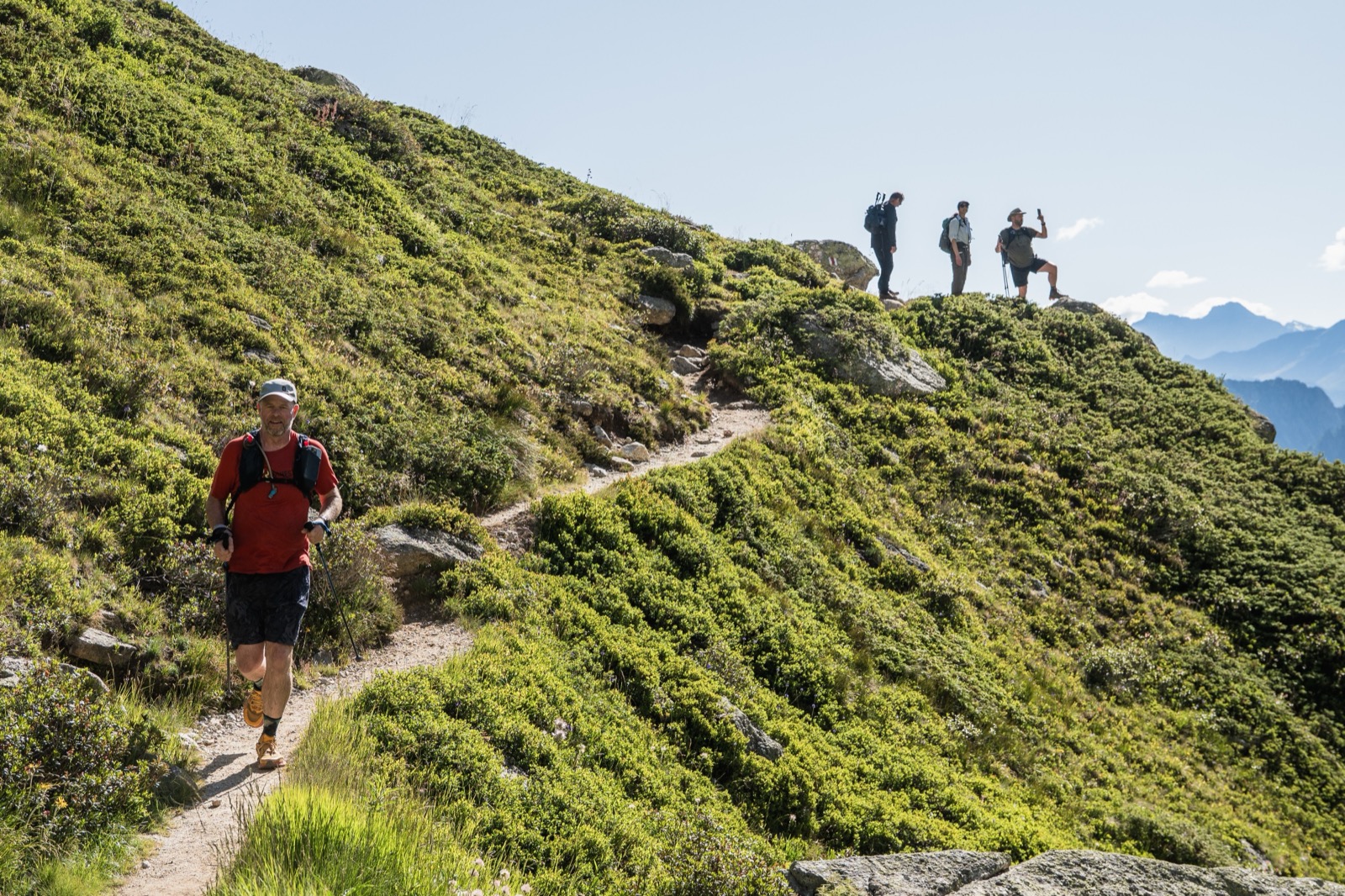 Runners on a grassy ridgeline trail, with others waiting on the crest above