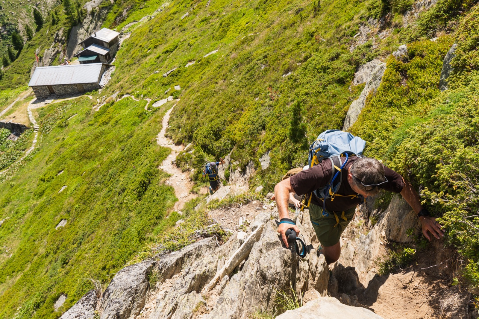Runner climbing a steep rocky section above a mountain hut