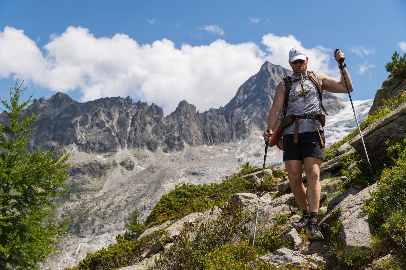 Runner with poles on a rocky trail beneath jagged granite peaks
