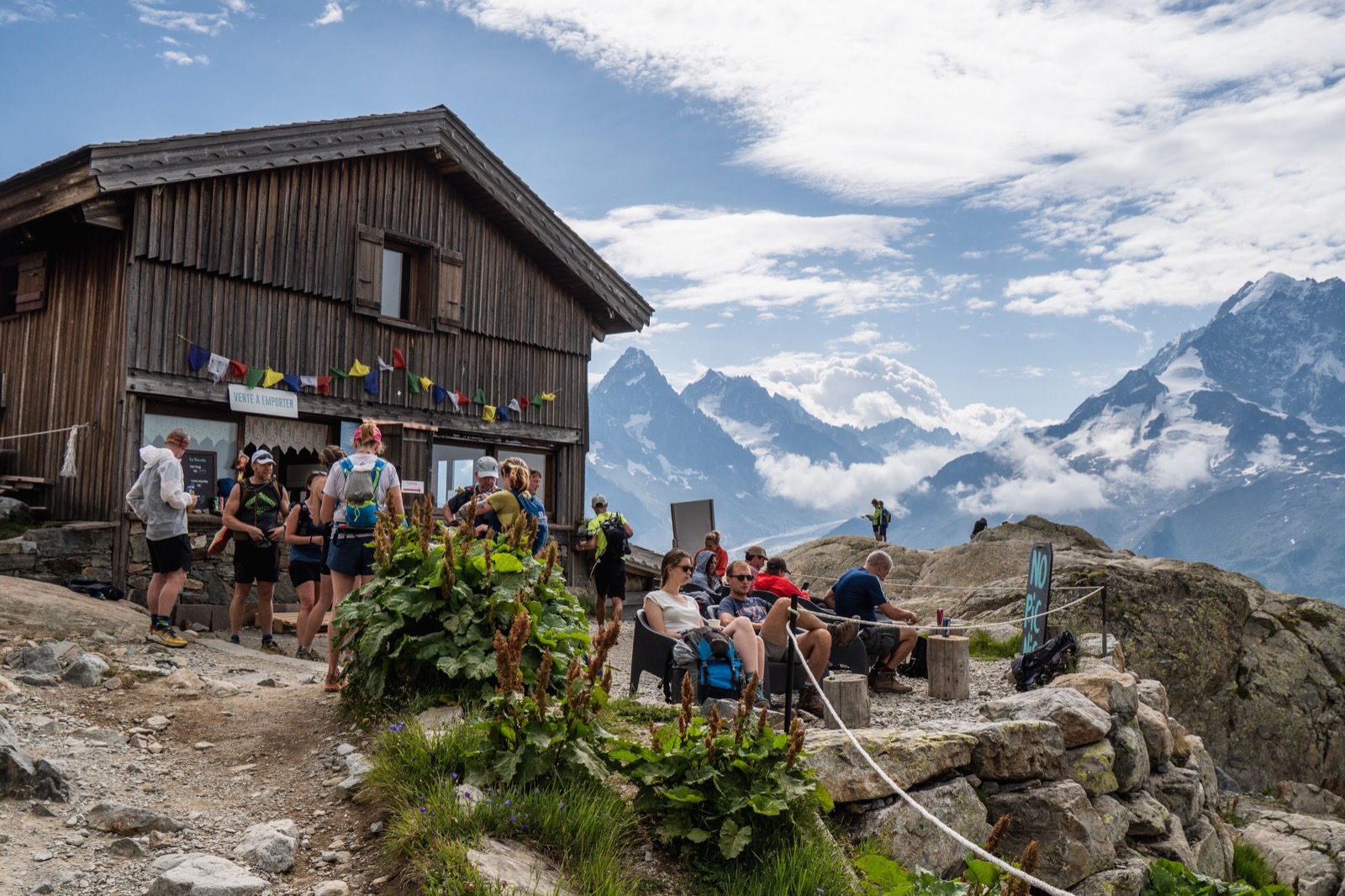 Runners gathered outside a mountain refuge with snowy peaks behind