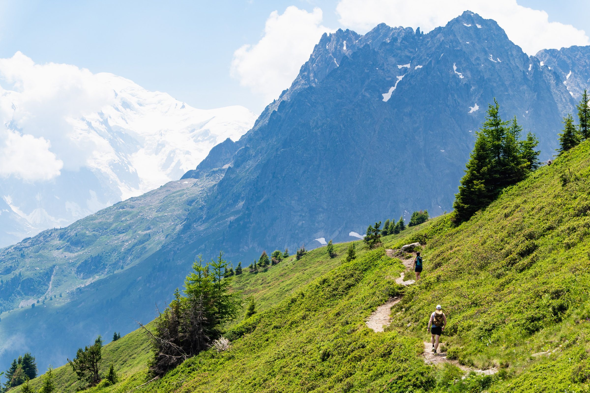 Trail runners on a mountain path in the Chamonix valley, with the Mont Blanc massif behind them